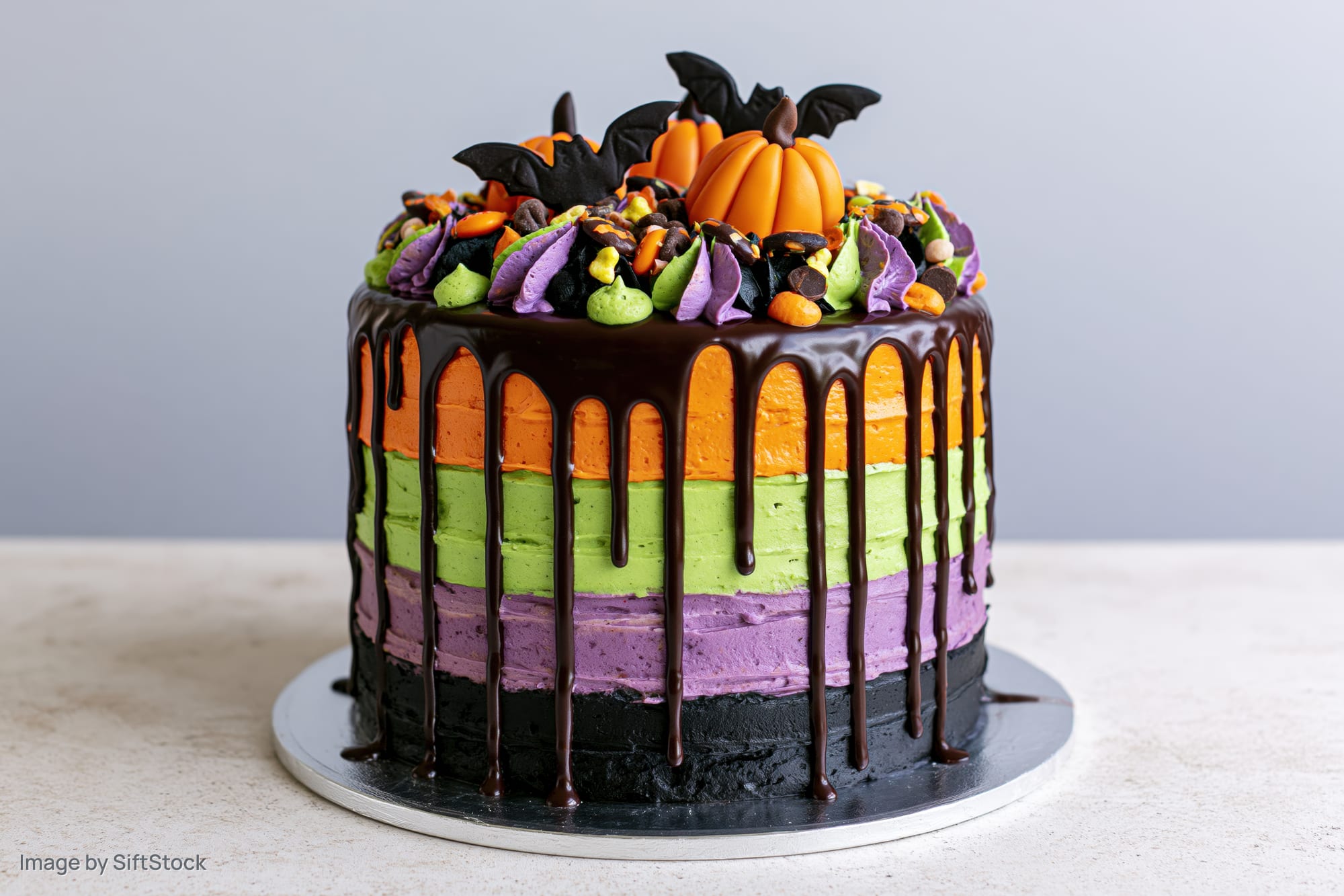 Halloween layer cake with dripping chocolate ganache and pumpkin bat decorations on a stand