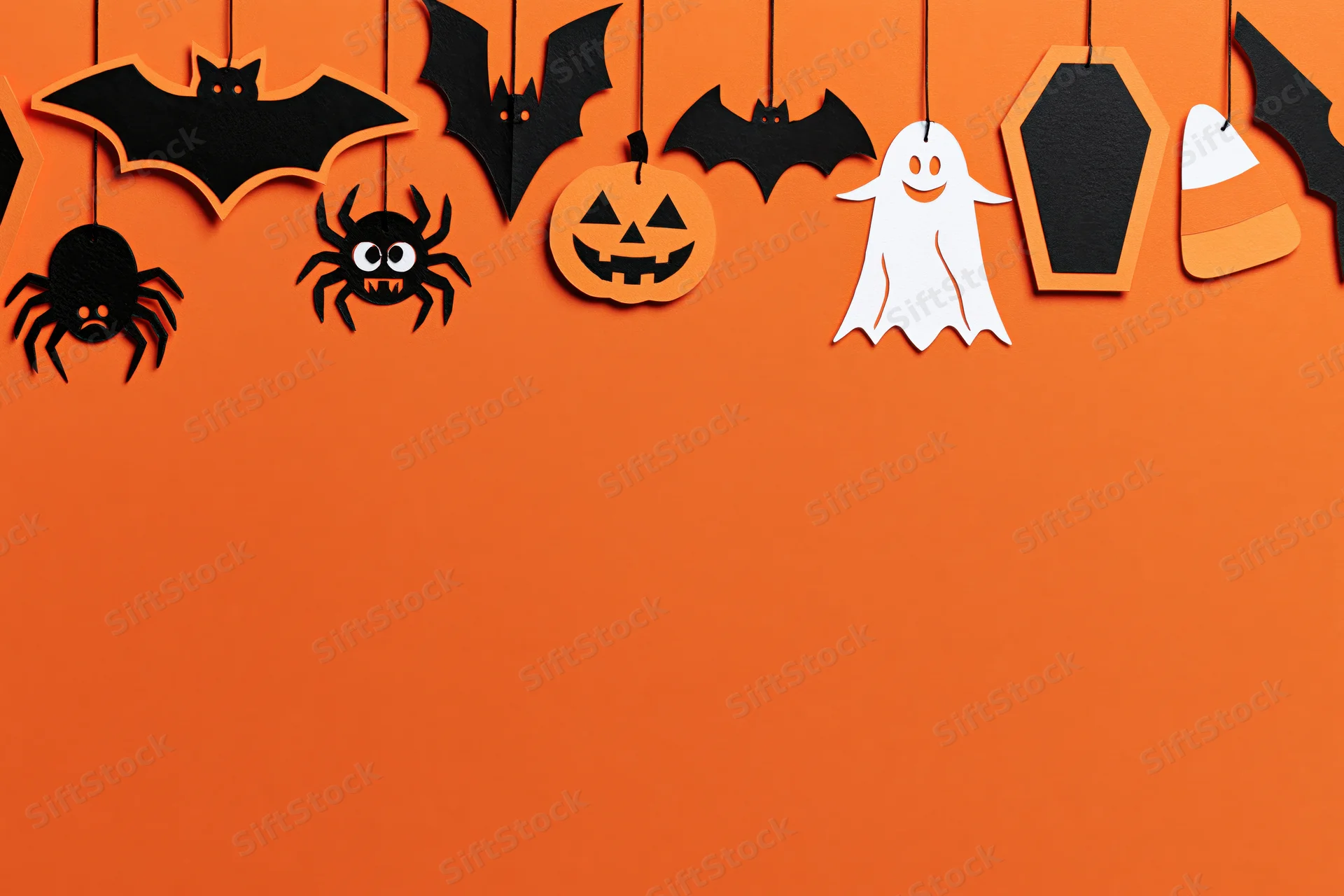 Halloween paper craft decorations hanging from strings across orange wall with copyspace below