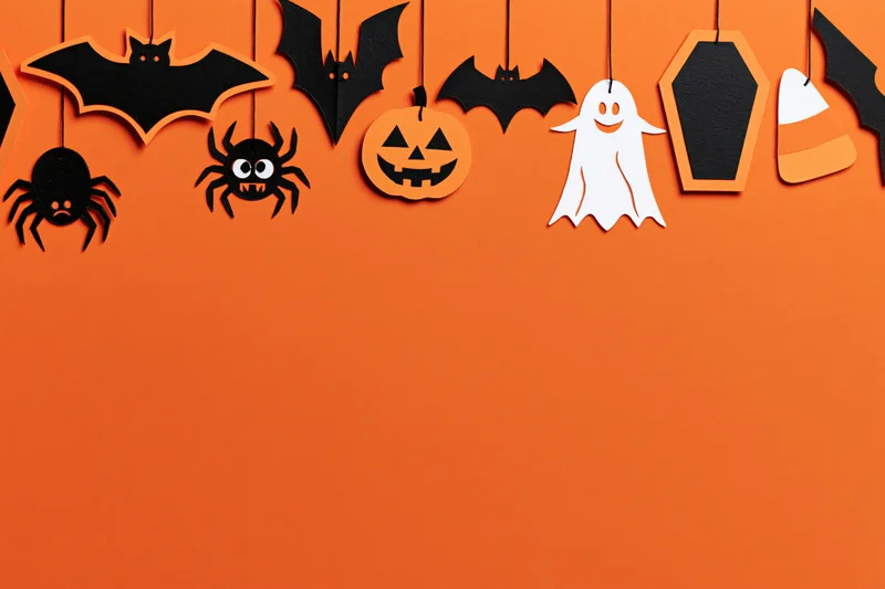 Halloween paper craft decorations hanging from strings across orange wall with copyspace below