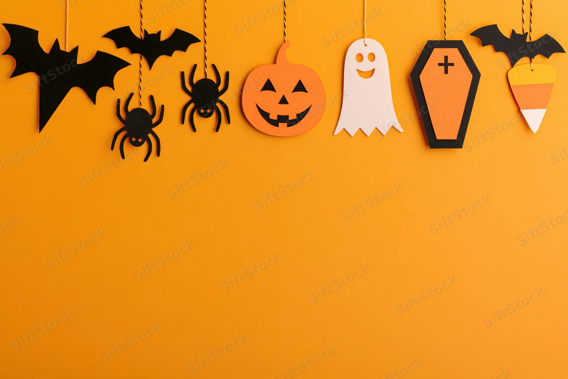 Halloween paper decorations hanging in a row across an orange wall with copyspace below