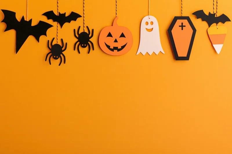 Halloween paper decorations hanging in a row across an orange wall with copyspace below