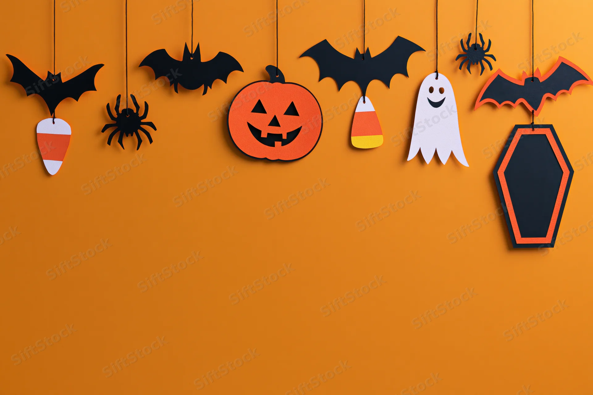 Halloween paper craft decorations hanging from strings across an orange wall with copyspace below