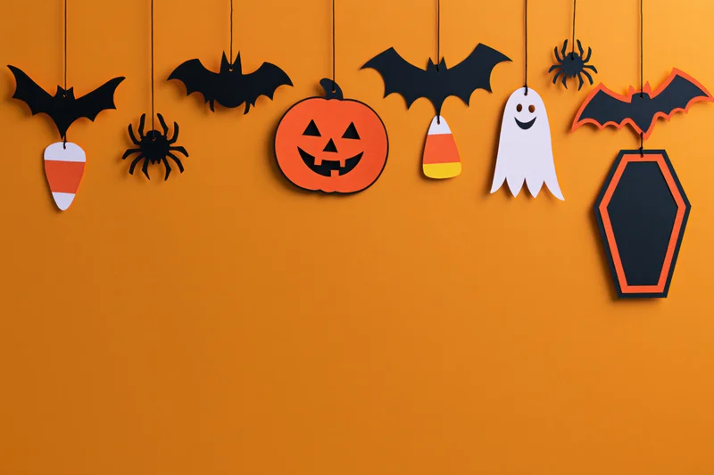 Halloween paper craft decorations hanging from strings across an orange wall with copyspace below