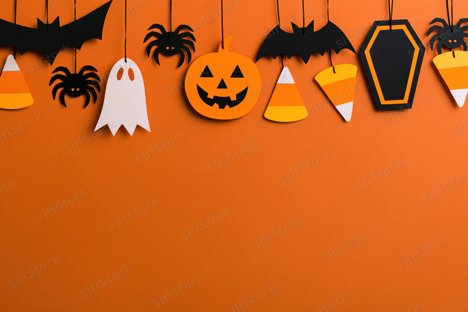 Halloween paper craft decorations hanging from strings across orange wall with copyspace below