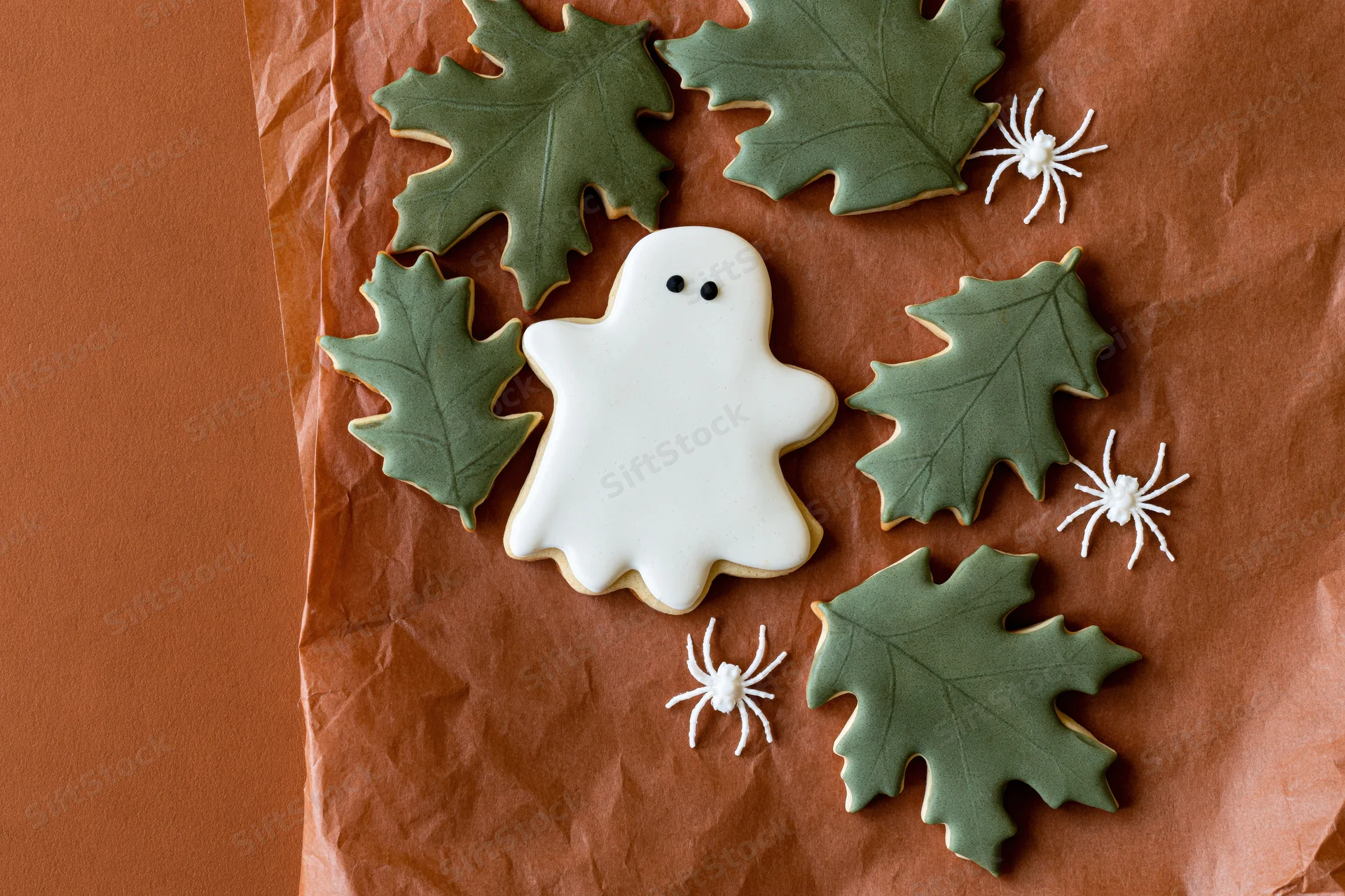 Halloween sugar cookies shaped as ghosts and leaves with white spiders arranged on crumpled brown paper