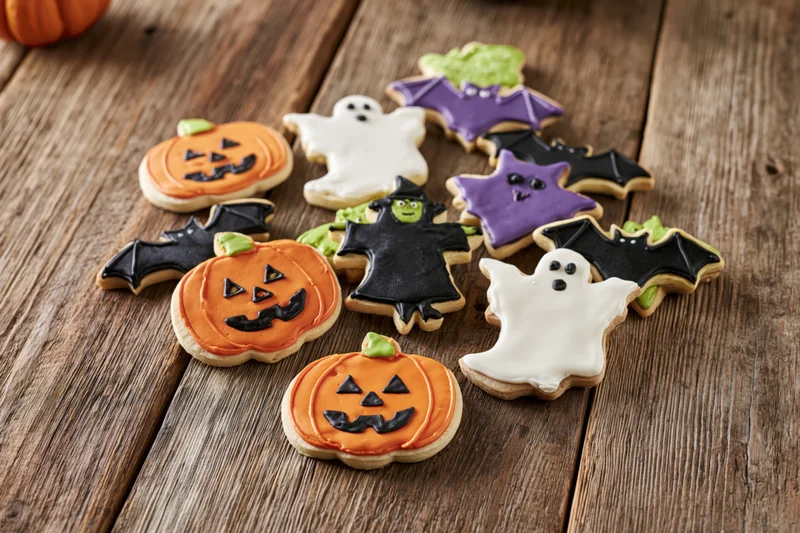 Halloween sugar cookies shaped as pumpkins ghosts bats and witches arranged on a rustic wooden table