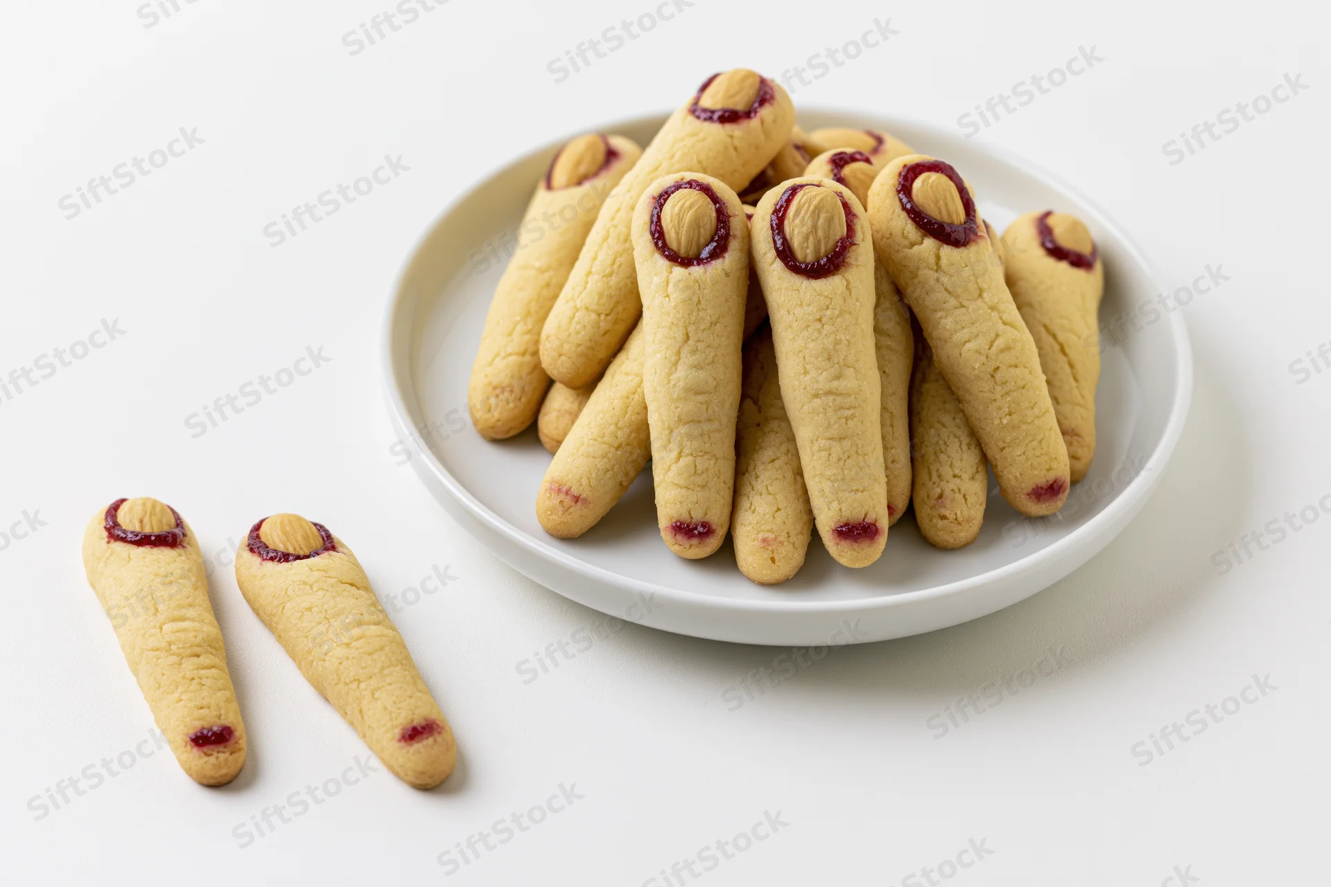 Witch finger cookies piled on a white ceramic plate with two cookies beside it