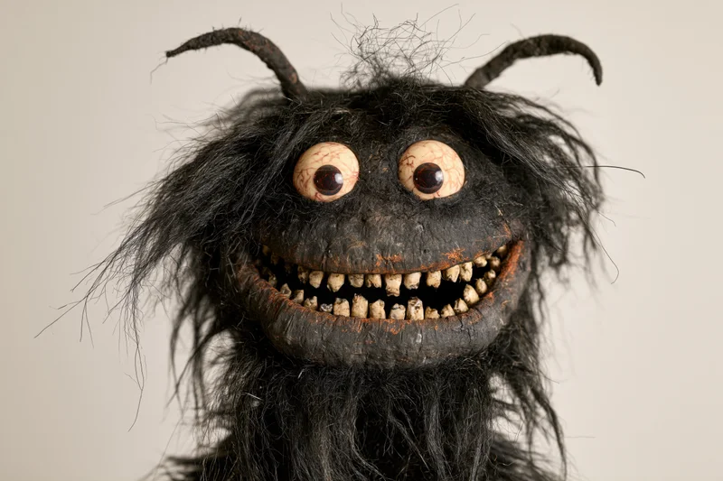Handmade monster puppet with wild black fur, bulging bloodshot eyes, and jagged teeth, isolated on plain background