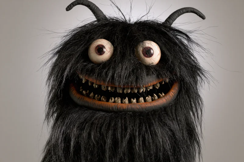 Closeup of handmade monster puppet with wild black fur, bulging bloodshot eyes, and sharp teeth in a wide grin
