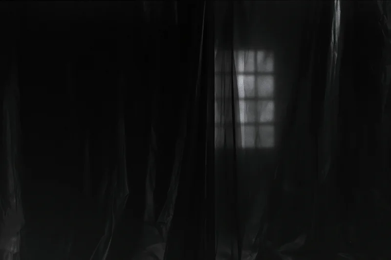 Dark plastic sheeting hanging in vertical folds inside a dim interior with light filtering through a window