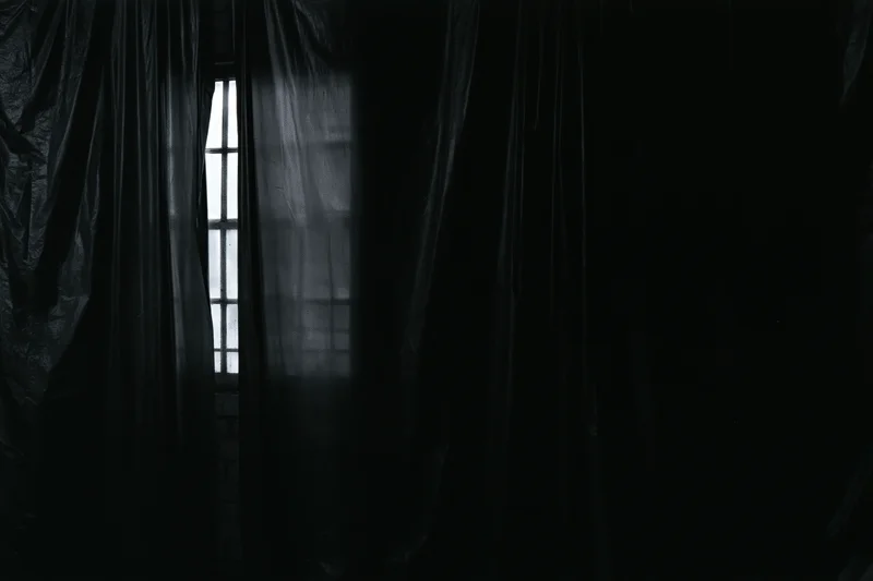 Dark plastic sheeting hanging in vertical folds inside a dim interior with light filtering through a window