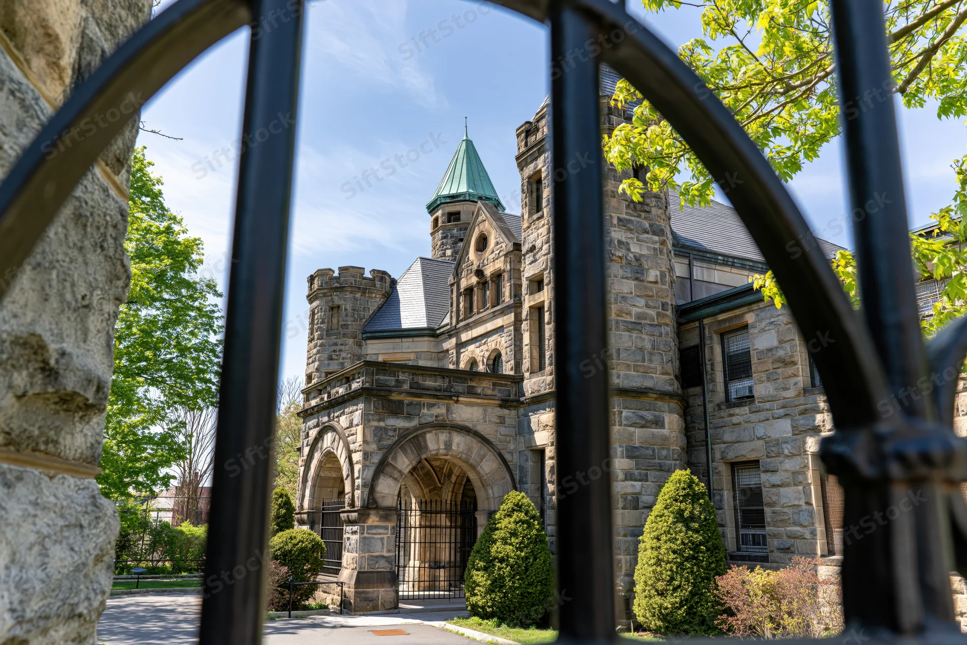 Stone prison building with arched entrance and turret viewed through iron gate on sunny day