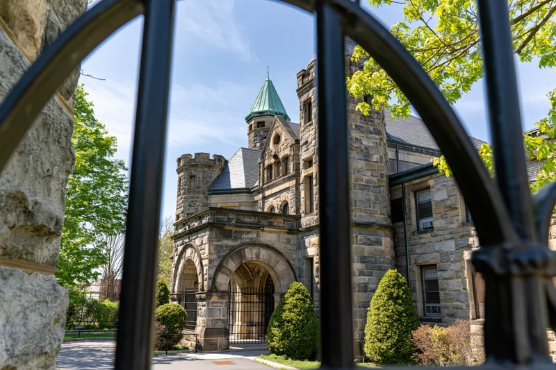 Stone prison building with arched entrance and turret viewed through iron gate on sunny day