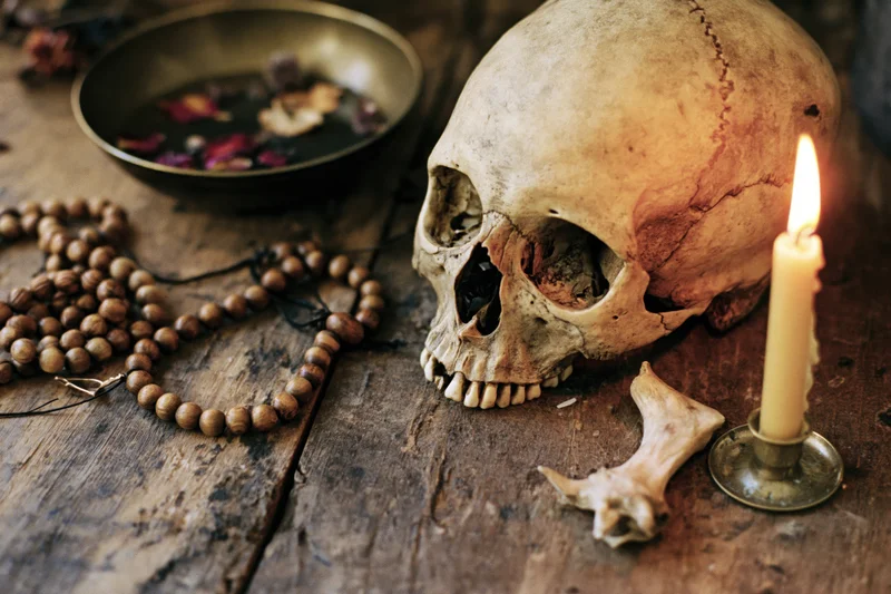 Human skull with lit candle and ritual objects on wooden table