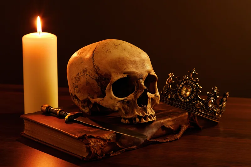 Human skull resting on an aged leather-bound book beside a lit candle and ornate crown on a wooden table