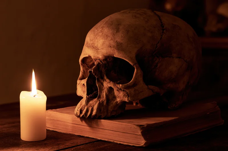 Human skull resting on an old worn book beside a lit candle on a wooden table