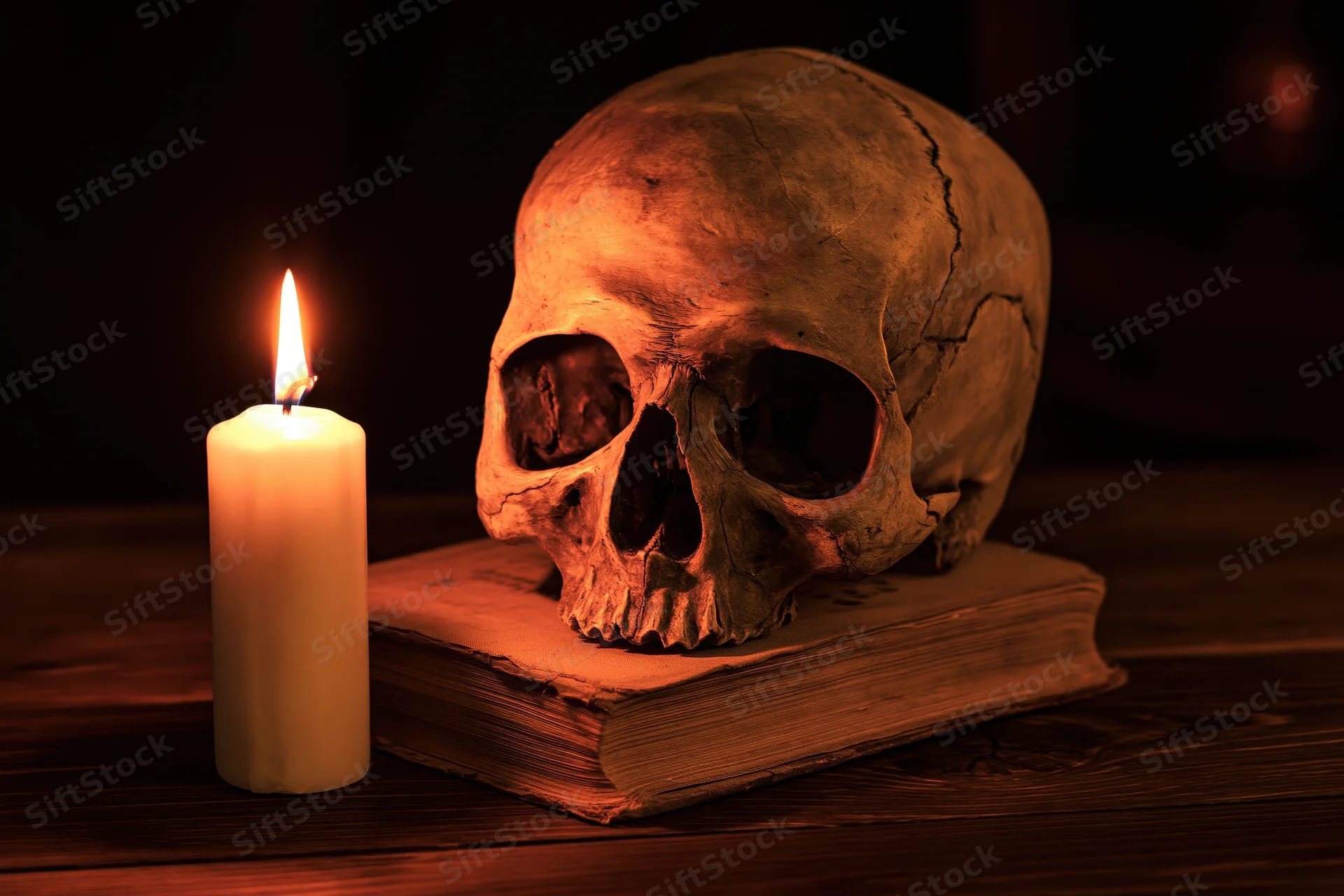 Human skull resting on an old worn book beside a lit candle on a wooden table