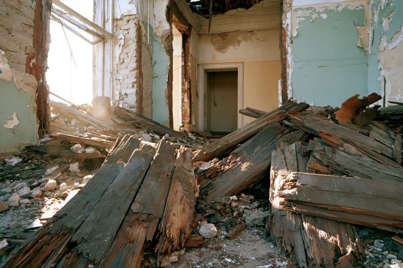 Collapsed interior of abandoned building with debris and broken wood beams scattered across floor