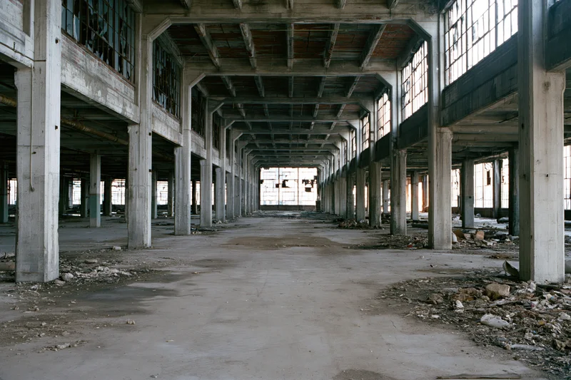 Empty interior of abandoned industrial warehouse with concrete pillars and broken windows