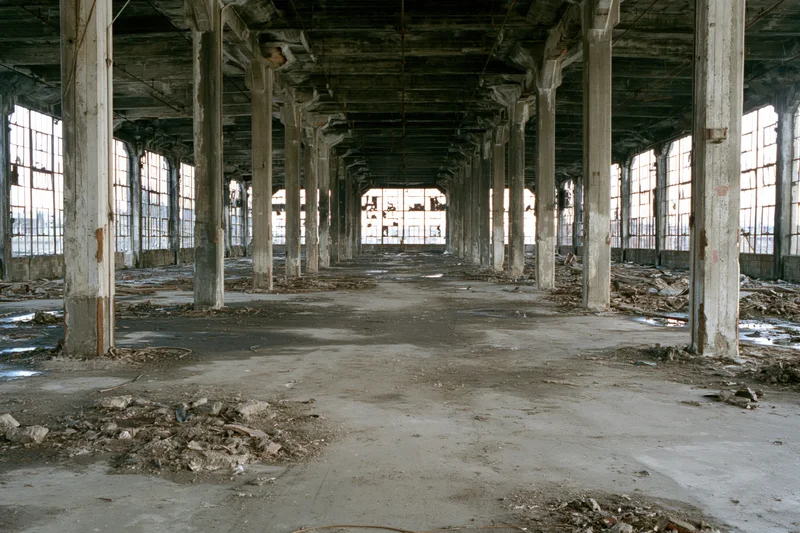 Empty interior of abandoned industrial warehouse with concrete pillars and debris on floor