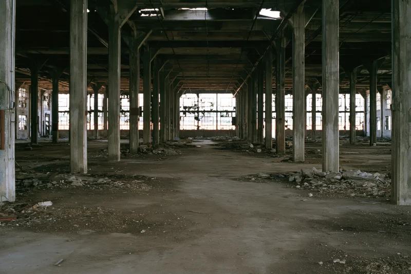 Vast empty interior of abandoned industrial warehouse with concrete pillars and broken windows