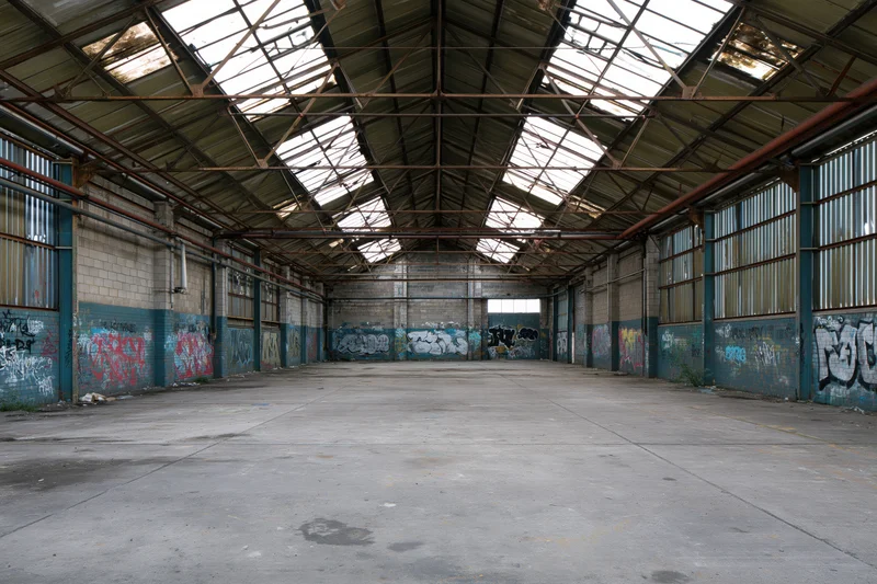 Empty interior of abandoned industrial warehouse with graffiti-covered walls and skylight ceiling