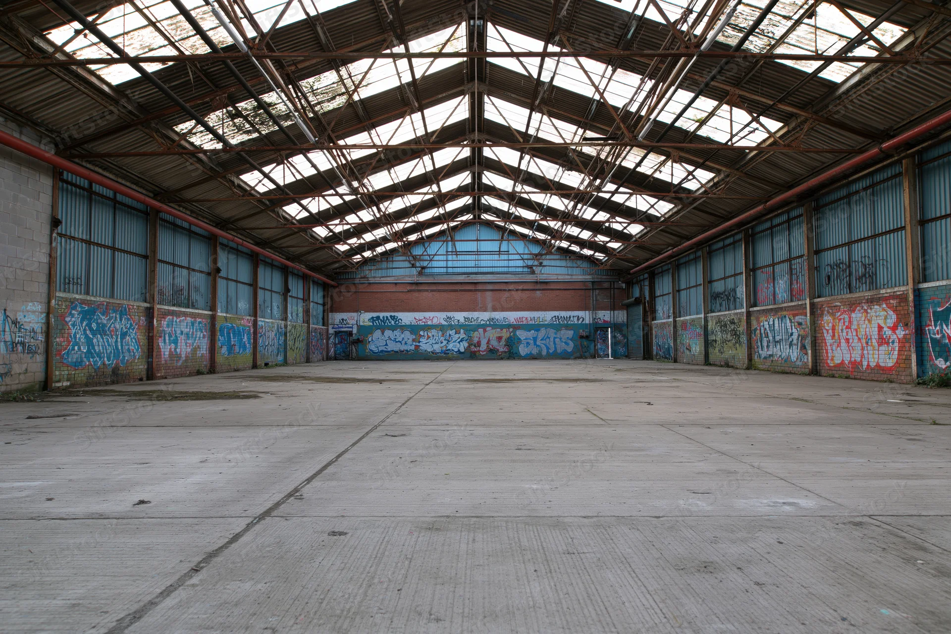 Empty interior of abandoned industrial warehouse with graffiti-covered walls and metal roof structure