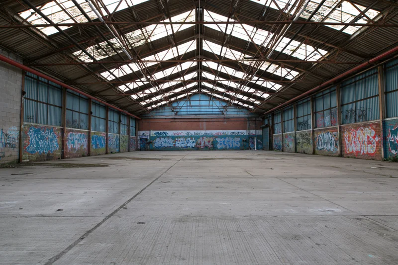 Empty interior of abandoned industrial warehouse with graffiti-covered walls and metal roof structure