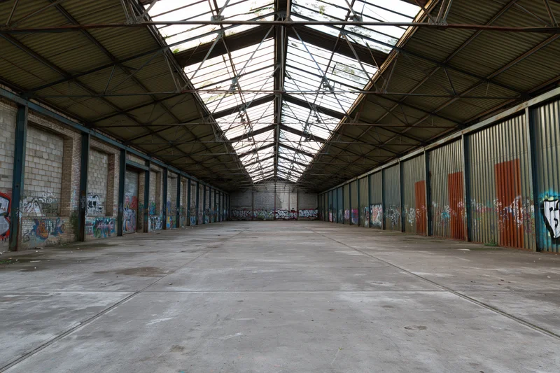 Empty interior of abandoned industrial warehouse with graffiti-covered walls and metal roof structure