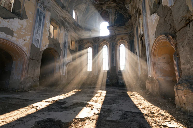 Sunbeams streaming through broken windows in the empty nave of an abandoned baroque church