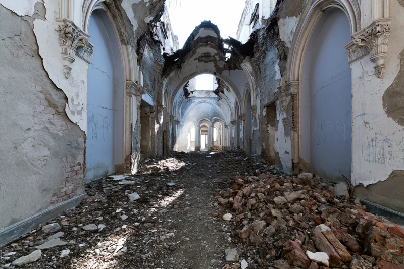 Crumbling hallway with gothic arches and rubble under daylight