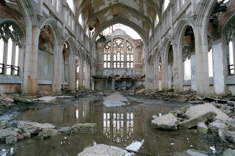 Interior of abandoned gothic church nave with broken windows and water puddles reflecting stone arches
