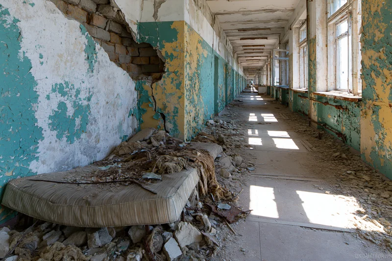 Long hallway in abandoned soviet-era building with peeling paint and discarded mattress among rubble