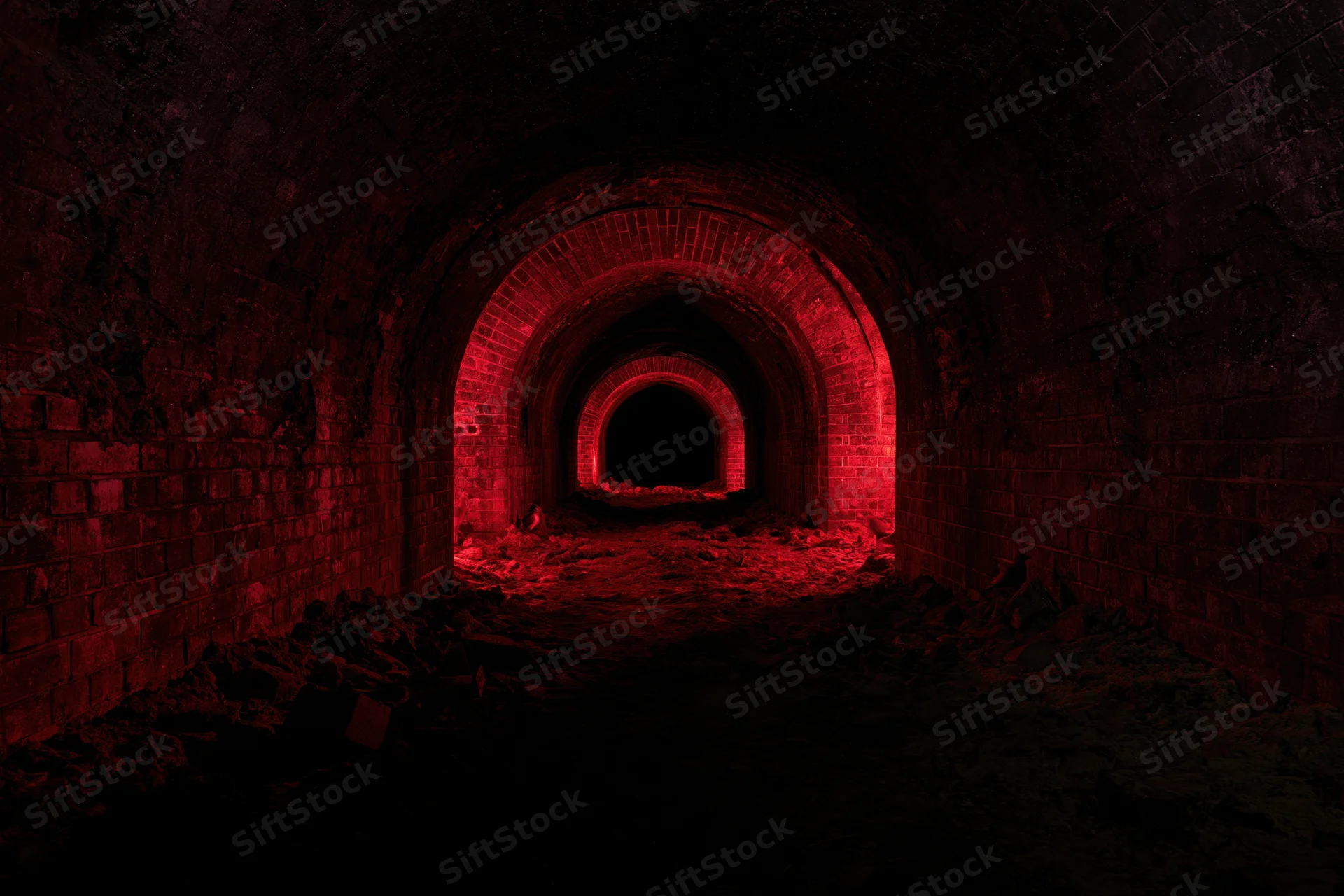 Dark red-lit arched brick tunnel with rubble inside abandoned underground cellar
