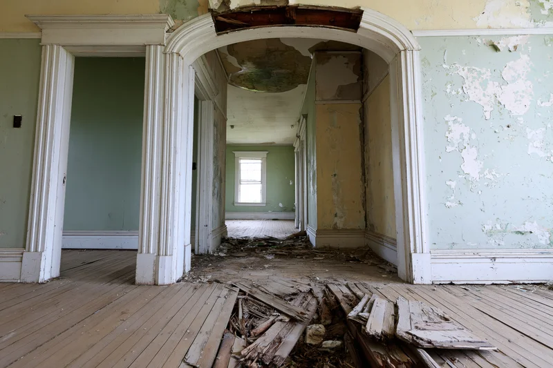 Abandoned house interior with broken floor and peeling paint visible through arched doorway