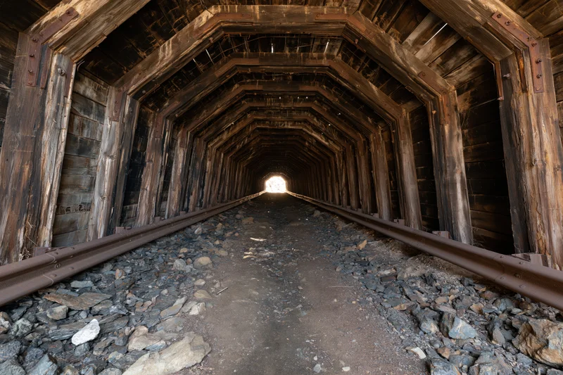 Interior of an abandoned wooden railway tunnel with tracks receding into light at the far end