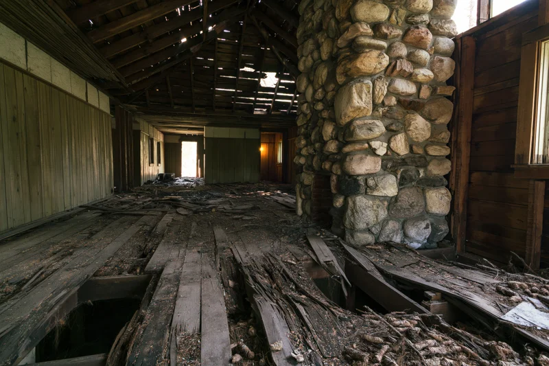 Interior of abandoned wooden building with broken floor and stone pillar, showing decay and structural damage