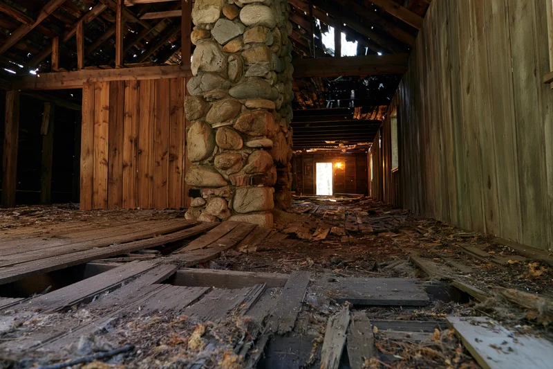 Interior of abandoned wooden building with broken floor and stone chimney, wide-angle ground-level view