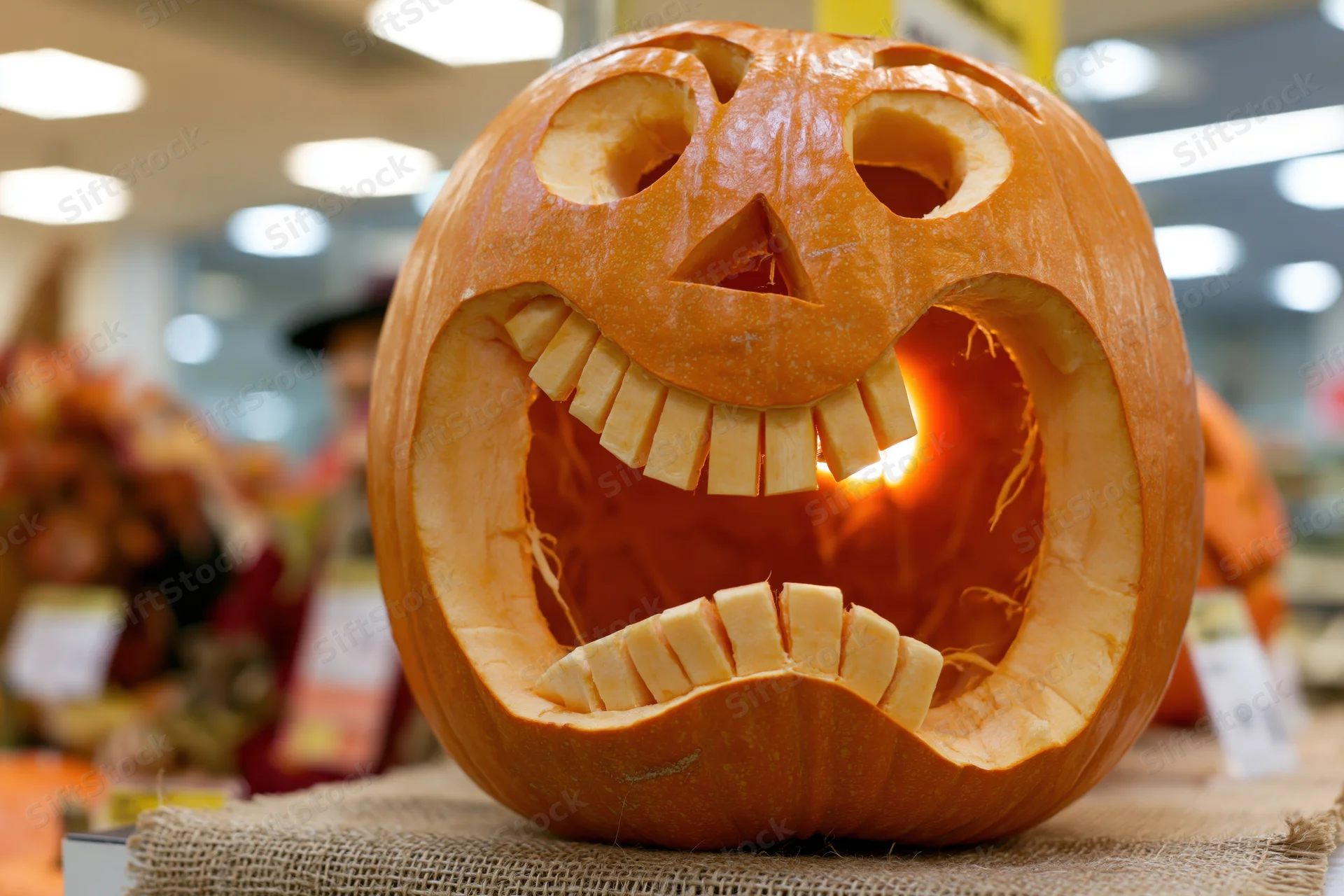 Carved pumpkin with glowing teeth smile displayed on burlap in store