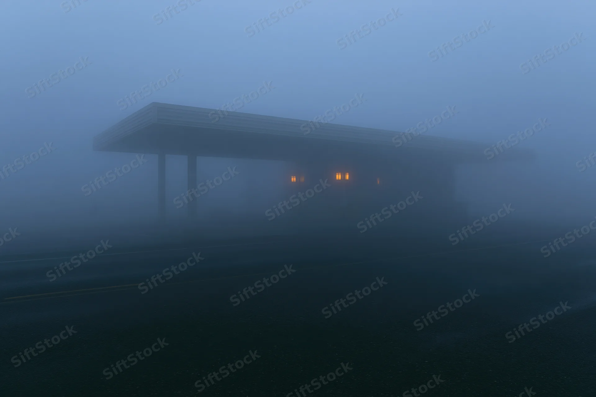 Isolated roadside building with covered canopy in dense fog at twilight