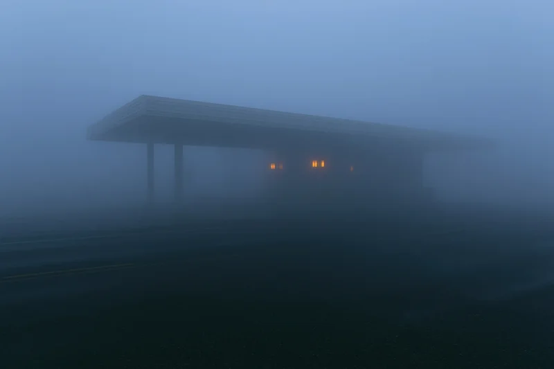 Isolated roadside building with covered canopy in dense fog at twilight