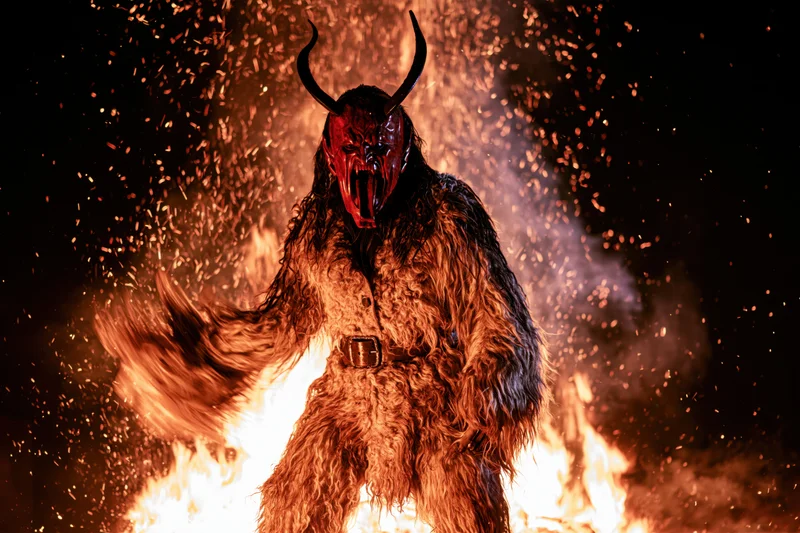 Krampus figure in fur costume with red mask and horns roaring amidst flames and sparks at night