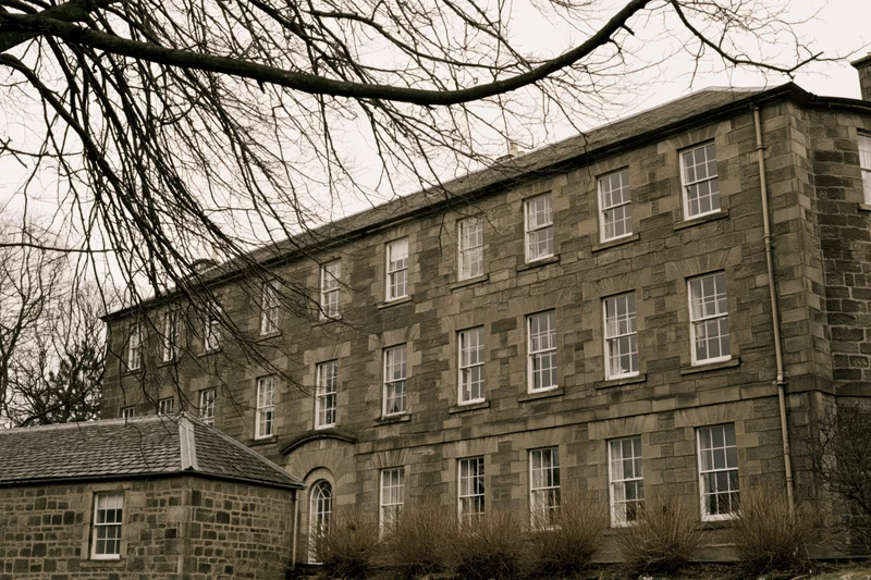 Large georgian stone manor building with multiple sash windows and bare trees in front on an overcast day