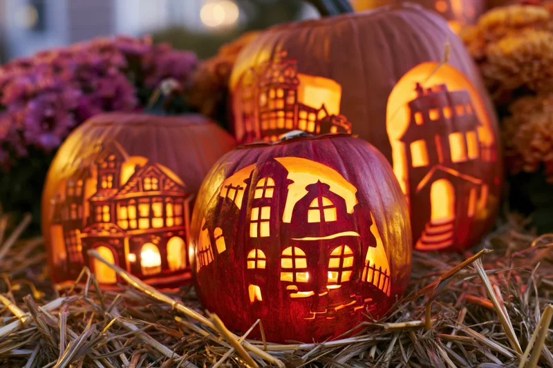 Carved pumpkins with intricate haunted house designs glowing on straw at night