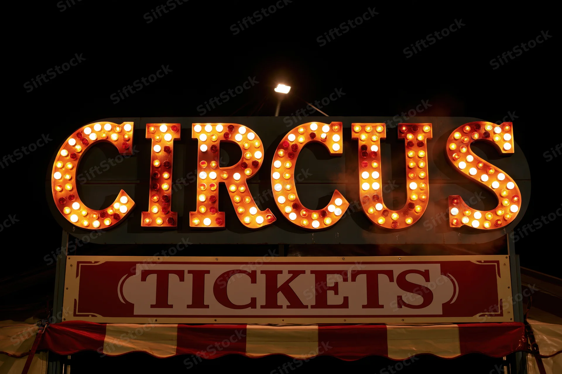 Illuminated circus marquee sign with bulbs and tickets banner at night