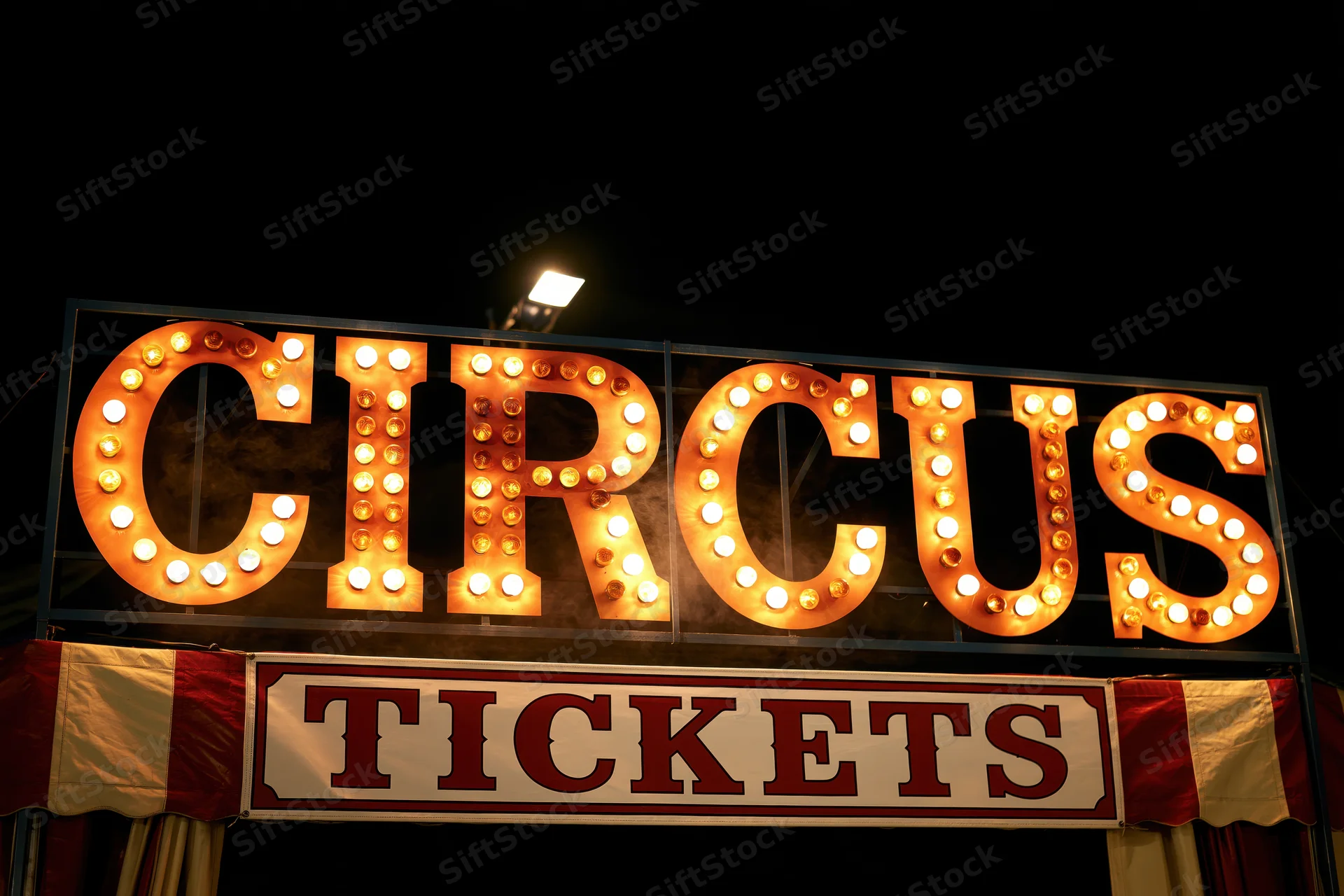 Illuminated circus marquee sign with bulbs and tickets banner at night