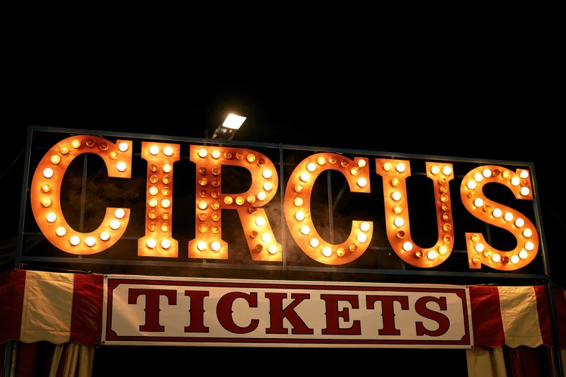 Illuminated circus marquee sign with bulbs and tickets banner at night