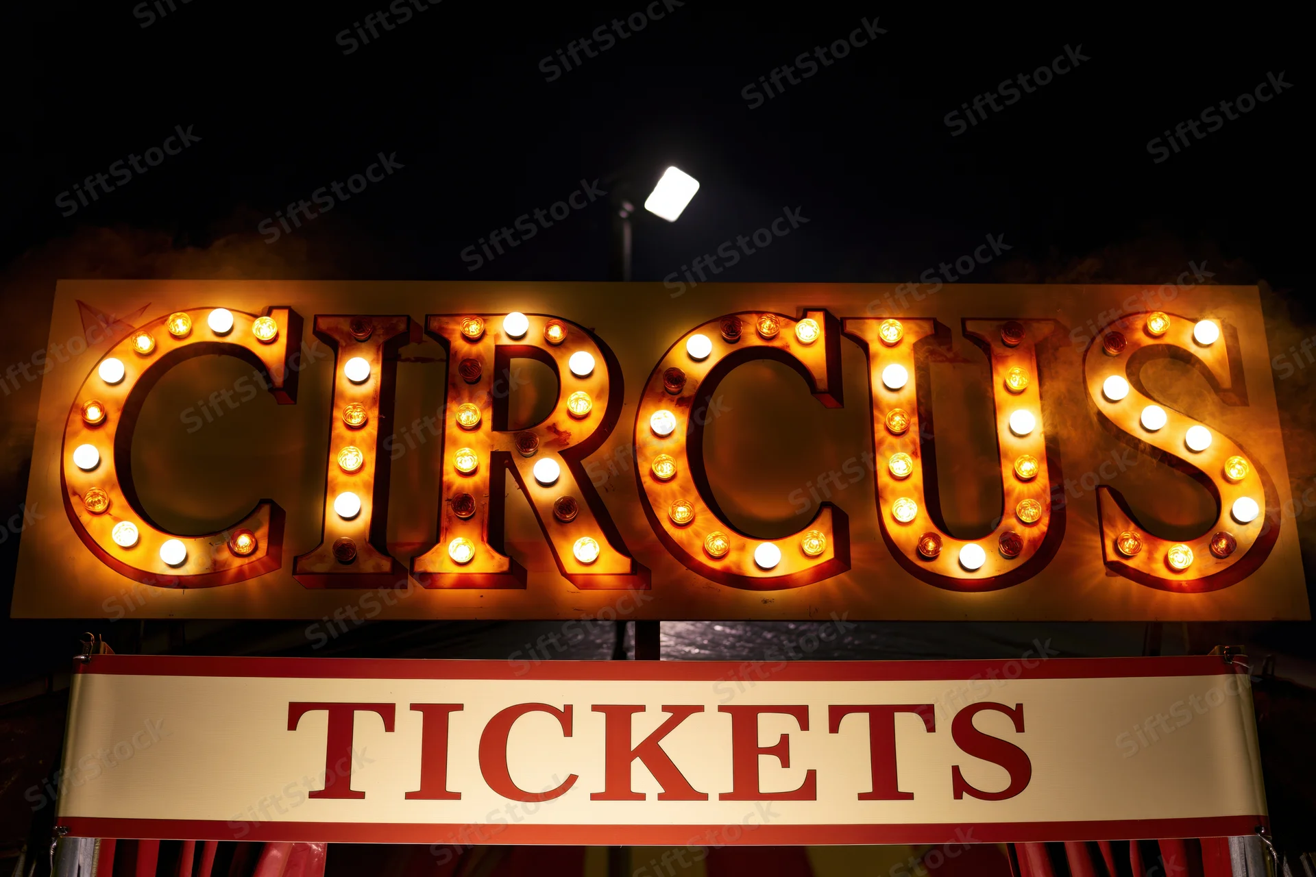 Illuminated circus marquee sign with round bulbs at night above a tickets banner