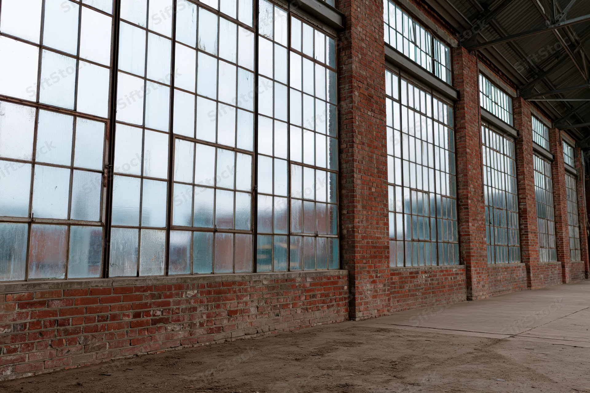 Interior of empty industrial warehouse with tall multi-paned windows and brick walls