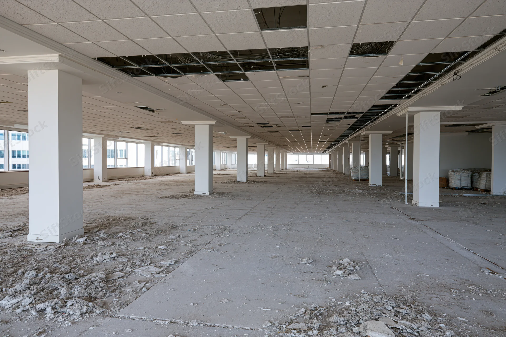 Large vacant commercial office space mid-renovation with exposed ceiling wiring and concrete floor debris